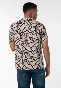 Kurzarmhemd aus beigem Stoff mit einem schwarzen abstrakten Muster. Hat einen lässigen Schnitt und einen klassischen Kragen. Rückansicht, getragen mit blauen Jeans.