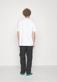 Witte korte mouwen t-shirt, ontspannen pasvorm, gecombineerd met donkergrijze broek met een zijzak en groene sneakers. Minimalistisch ontwerp.