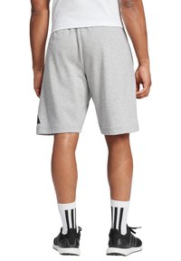 Shorts de sport en coton gris avec une taille élastique. Inclut des accents géométriques noirs sur les côtés. Portés avec des chaussures noires et des chaussettes rayées.