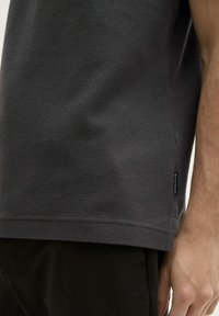 Grå tekstureret t-shirt med korte ærmer, der har et lille mærkelabel ved kanten og en afslappet pasform.