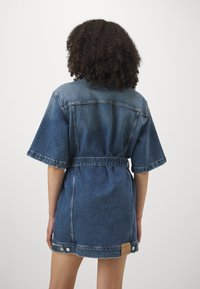Denim dress with short, wide sleeves, belted waist, and raw hem. Features a leather label and contrasting stitching in dark blue.