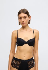 Černá podprsenka s vycpávkami a krajkovými detaily, nastavitelné ramínka a hladká látka. Kombinujte s odpovídajícím černým spodním prádlem s krajkovými doplňky.