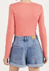 Long-sleeve, ribbed, coral top paired with high-waisted, light blue denim shorts featuring rolled cuffs and two back pockets.