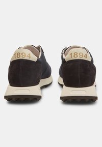 Crne suede i mrežaste tenisice s bijelim potplatima. Stražnji dio sadrži bež petni dio s oznakom "1894" u zlatnoj boji. Gumeni potplat s reljefom za bolje prianjanje.