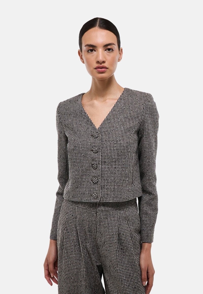 Blazer noir et blanc à motif pied de poule avec un col en V, des manches longues et cinq boutons. Tissu texturé avec une coupe ajustée.