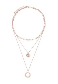Collier superposé en or rose comprenant trois chaînes : une avec un pendentif en forme de rayons de soleil, une avec un charm circulaire texturé, et une chaîne délicate.
