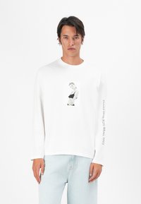 Witte langemouw t-shirt met een zwart-wit fotoafdruk op de voorkant, met "David Sims Kate Moss, 1993" op de mouw gedrukt.