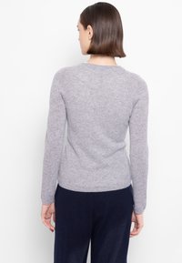 Maglione grigio lavorato a maglia con maniche lunghe, scollo rotondo, taglio aderente e tessuto morbido, abbinato a pantaloni scuri, visto da dietro.