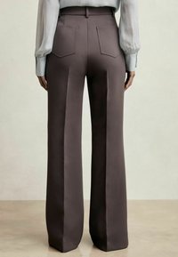 Pantaloni a vita alta e gamba larga in tessuto marrone scuro. Presentano due tasche posteriori e una texture liscia. Abbinati a una camicetta blu chiaro.