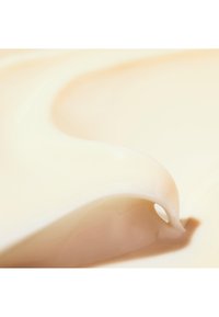 Romige beige substantie met een zachte, vloeiende textuur, subtiele glans en zachte rondingen, met een kleine opening in één gedeelte.