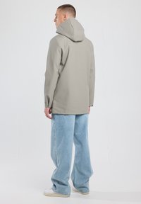 Light gray waterproof jacket with a hood, long sleeves, and a relaxed fit, paired with blue wide-leg jeans and white sneakers.