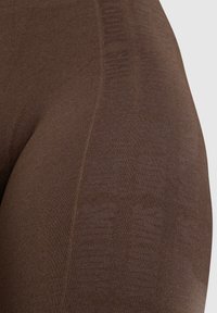 Bruine leggings van rekbare stof, met een gestructureerd patroon en een strak ontwerp met naden langs de zijkanten.