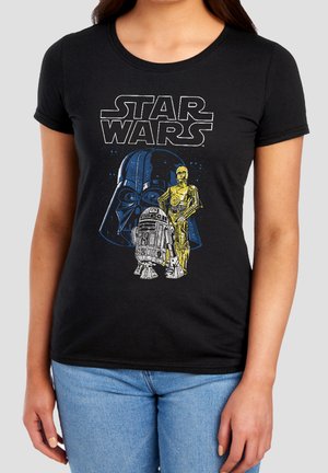 Frau trägt ein schwarzes Star Wars T-Shirt mit Bildern von Darth Vader, C-3PO und R2-D2 auf der Vorderseite.