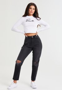 Valge lühendatud pikakä sleeves top musta kirjatööga, kombineeritud kõrge vöökohaga mustade teksadega, millel on rebenenud põlved ja valged tossud.
