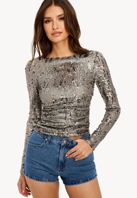 Top en sequins argentés brillants à manches longues avec un col rond, associé à un short en denim bleu. Il présente un design ajusté et une surface texturée.