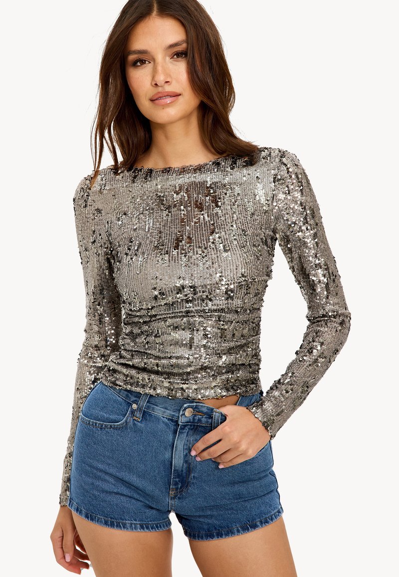 Top en sequins argentés brillants à manches longues avec un col rond, associé à un short en denim bleu. Il présente un design ajusté et une surface texturée.