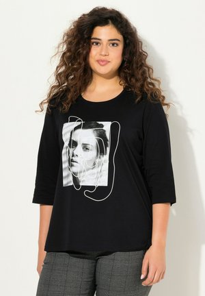 Schwarzes Baumwoll-T-Shirt mit einem Frontdruck, der ein Foto und ein Design aus weißen Linien zeigt. Mit Dreiviertelärmel und lässigem Schnitt.