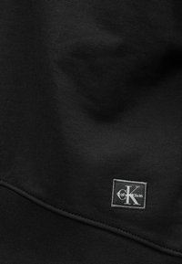 Μαύρο φούτερ από απαλό βαμβακερό μείγμα, με γκρι κεντημένη ετικέτα λογότυπου που φέρει το "Calvin Klein" και ανάγλυφο "CK" στο στήθος.