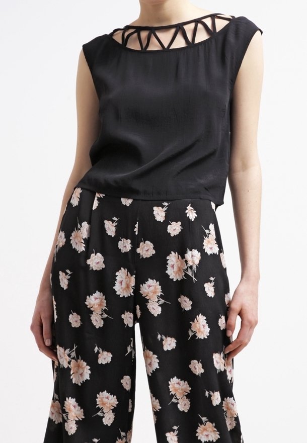 Top negro sin mangas con un diseño recortado alrededor del escote, combinado con pantalones de pierna ancha negros que presentan un patrón floral en rosa.