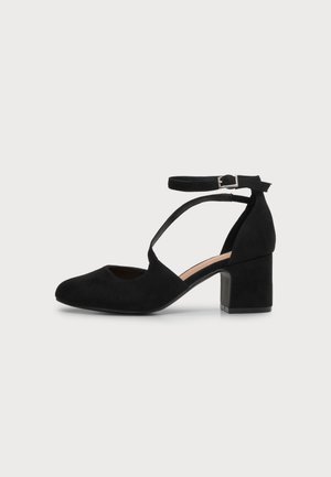 Escarpin Mary Jane noir en daim, à bout fermé, avec des brides croisées, une boucle à la cheville et un talon bloc épais.
