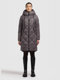 Woman wearing a long, quilted gray hooded coat with black zipper pockets, black tights, and black knee-high boots standing on a white background.