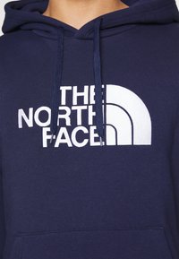 Felpa con cappuccio blu navy con logo bianco "THE NORTH FACE". Caratterizzata da cordini e una tasca frontale. Realizzata in un tessuto morbido e testurizzato.