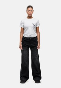 Witte t-shirt met vlinderafbeelding en tekst, gecombineerd met zwarte wijde jeans met kenmerkende stiksels en gebogen naaddetails.