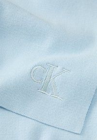 Tecido azul claro com uma textura nervurada, apresentando um logótipo bordado "cK" numa tonalidade ligeiramente mais escura, posicionado na parte inferior.