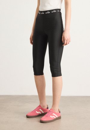 Leggings neri a tre quarti con alta vita e logo bianco. Tessuto liscio ed elastico con una silhouette aderente.
