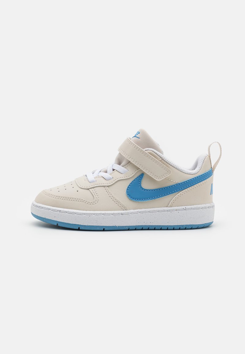 Baskets Nike en crème et bleu, avec une tige en cuir lisse, une sangle velcro, un système de laçage, un col rembourré et une semelle en caoutchouc texturée.