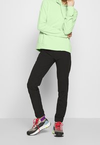 Sweat à capuche vert clair, pantalon slim noir et chaussures de sport multicolores avec lacets rouges. Caractérisé par un tissu lisse et une coupe moderne.