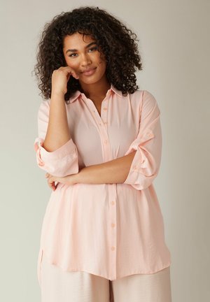 Camicia button-up rosa chiaro con vestibilità rilassata, maniche arrotolate e orlo curvo. Realizzata in un tessuto morbido e leggermente testurizzato.