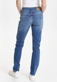 Jeans de mezclilla azul con corte recto, cinco bolsillos y un parche de cuero en la cinturilla. Un ligero desgaste añade textura.