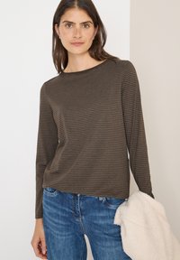 Brązowa, w paski, longsleeve z okrągłym dekoltem, wykonana z miękkiego materiału; noszona z niebieskimi dżinsami i trzymana biała, teksturowana odzież.