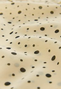 Látka s krémovým pozadím, na které jsou různě velké černé a šedé puntíky; hladká textura s lehkým splýváním.