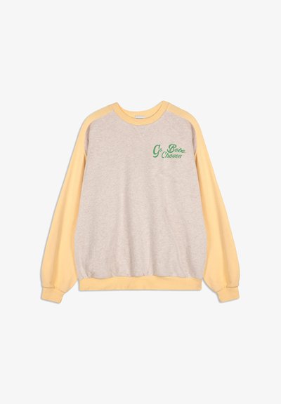 Sweatshirt ras du cou avec un corps beige et des manches jaune pastel, présentant du texte vert "Go Bobo Choses" sur le haut à gauche de la poitrine.