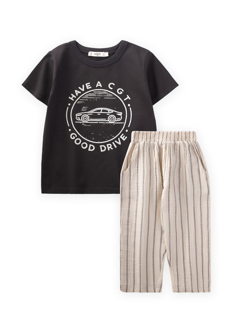 Camiseta de algodón negra con un gráfico de un coche blanco y el texto "TENGA UN CGT. BUEN VIAJE." combinada con pantalones de tiro ligero beige a rayas con cordón.