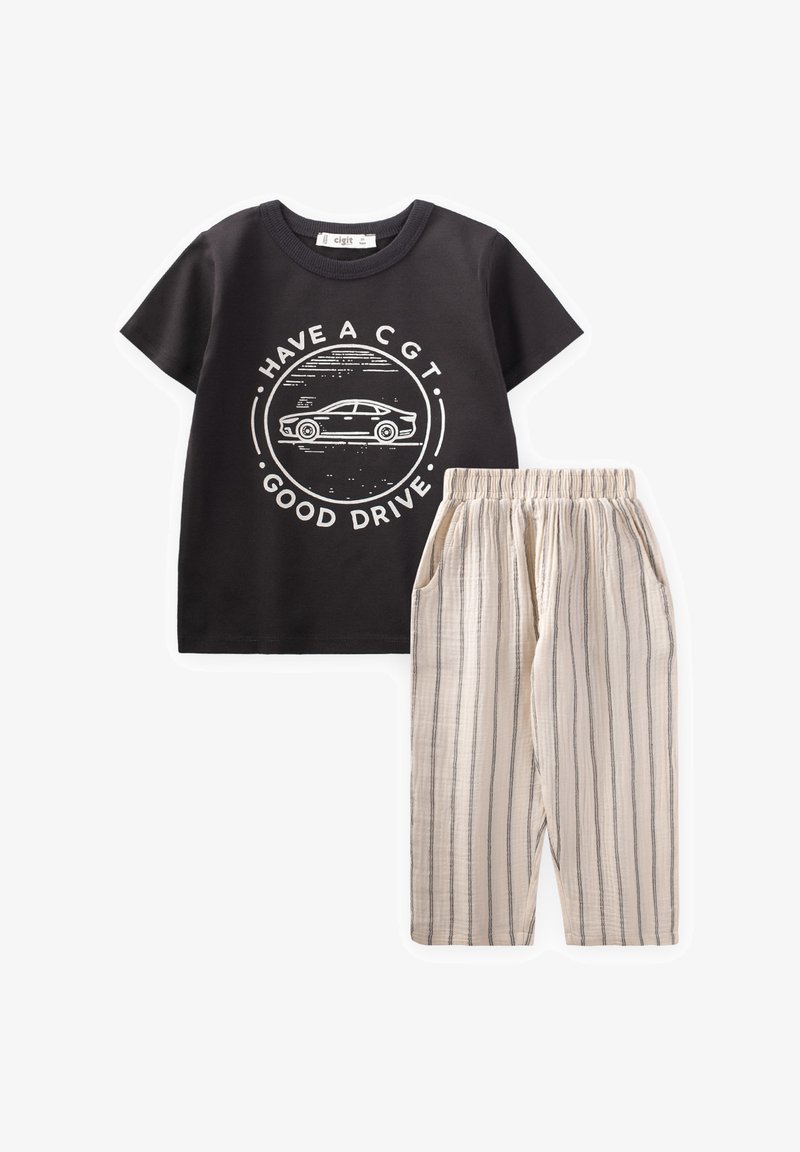Camiseta de algodón negra con un gráfico de un coche blanco y el texto "TENGA UN CGT. BUEN VIAJE." combinada con pantalones de tiro ligero beige a rayas con cordón.