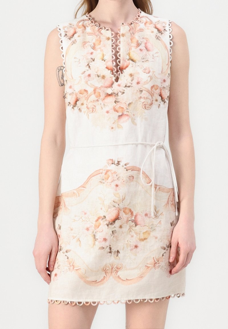 Robe blanche sans manches avec bords festonnés et motifs floraux rose pâle, avec un col en V et une fine ceinture nouée à la taille.
