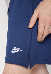 Pantalones cortos Nike azul marino fabricados con un tejido suave, con un logotipo bordado en blanco, costuras visibles y una abertura lateral en el dobladillo.