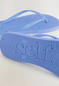 Mėlynos guminės šlepetės su tekstūruota padu, puoštos bangų raštu ir įspaustu žodžiu "self." ant pado.