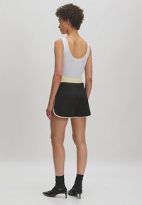 Shorts noirs avec une bordure jaune, associés à un débardeur blanc. Les shorts présentent une taille ajustée et un design global décontracté.