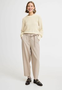 Pull en tricot crème avec un col rond associé à un pantalon beige taille haute avec une ceinture, complété par des mocassins noirs.
