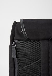 Black backpack featuring a durable canvas exterior, mesh paneling, leather accents, and a secure top flap with snap closure.