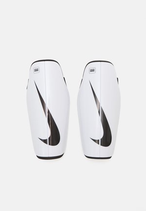White Nike shin guards with a black swoosh logo. Smooth plastic material, contoured design, rounded edges, and a small label on the top.