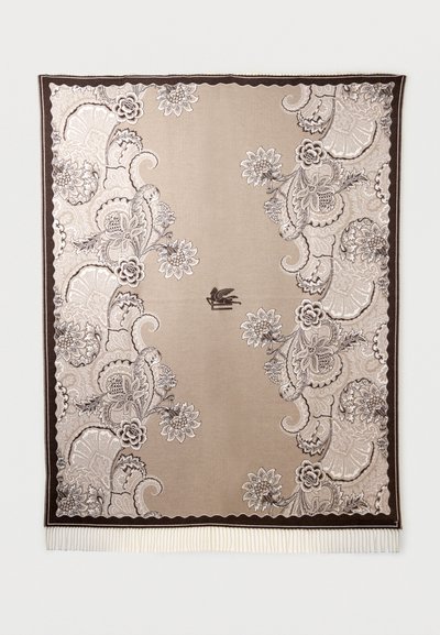 Textile à motifs floraux beige et marron avec des motifs paisley complexes, une bordure foncée, un emblème central de lion ailé, et une frange blanche sur le bord inférieur.