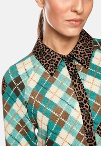 Figurbetontes Hemd mit einem tealfarbenen, braunen und weißen Argyle-Muster mit orangefarbenen Akzenten sowie einem Leopardenprint-Kragen. Mit Knopfleiste vorne.