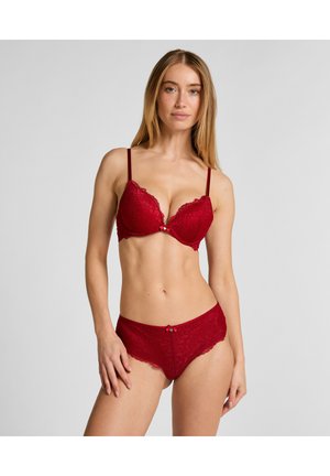Soutien-gorge en dentelle rouge et culottes assorties avec bords festonnés ; nœud décoratif au centre ; bretelles réglables ; texture transparente ; design moulant.