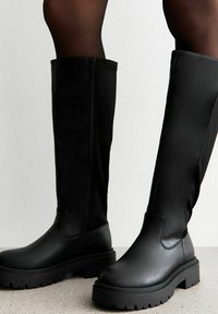 Zwarte kniehoge laarzen van soepel leer met een dikke zool en een zijrits. Voorzien van een ronde neus en een textiele rubberen buitenzool.