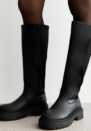 Zwarte kniehoge laarzen van soepel leer met een dikke zool en een zijrits. Voorzien van een ronde neus en een textiele rubberen buitenzool.